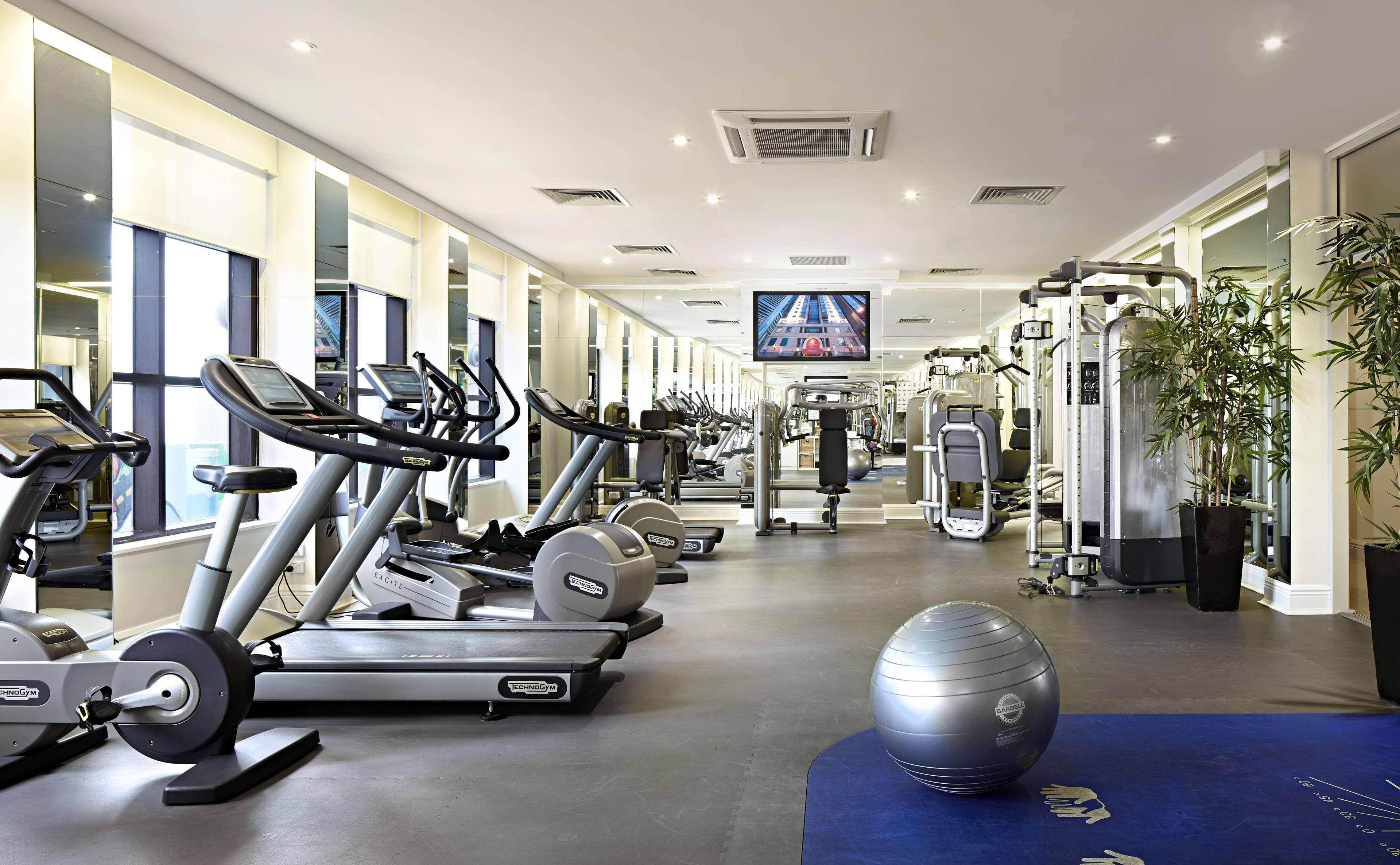 Hotel Stamford Plaza Ville de Melbourne Extérieur photo The photo shows a modern gym or fitness center. There are several exercise machines, including treadmills and elliptical trainers, positioned near large windows that allow natural light to flood the space. A television is mounted on the wall, likely 