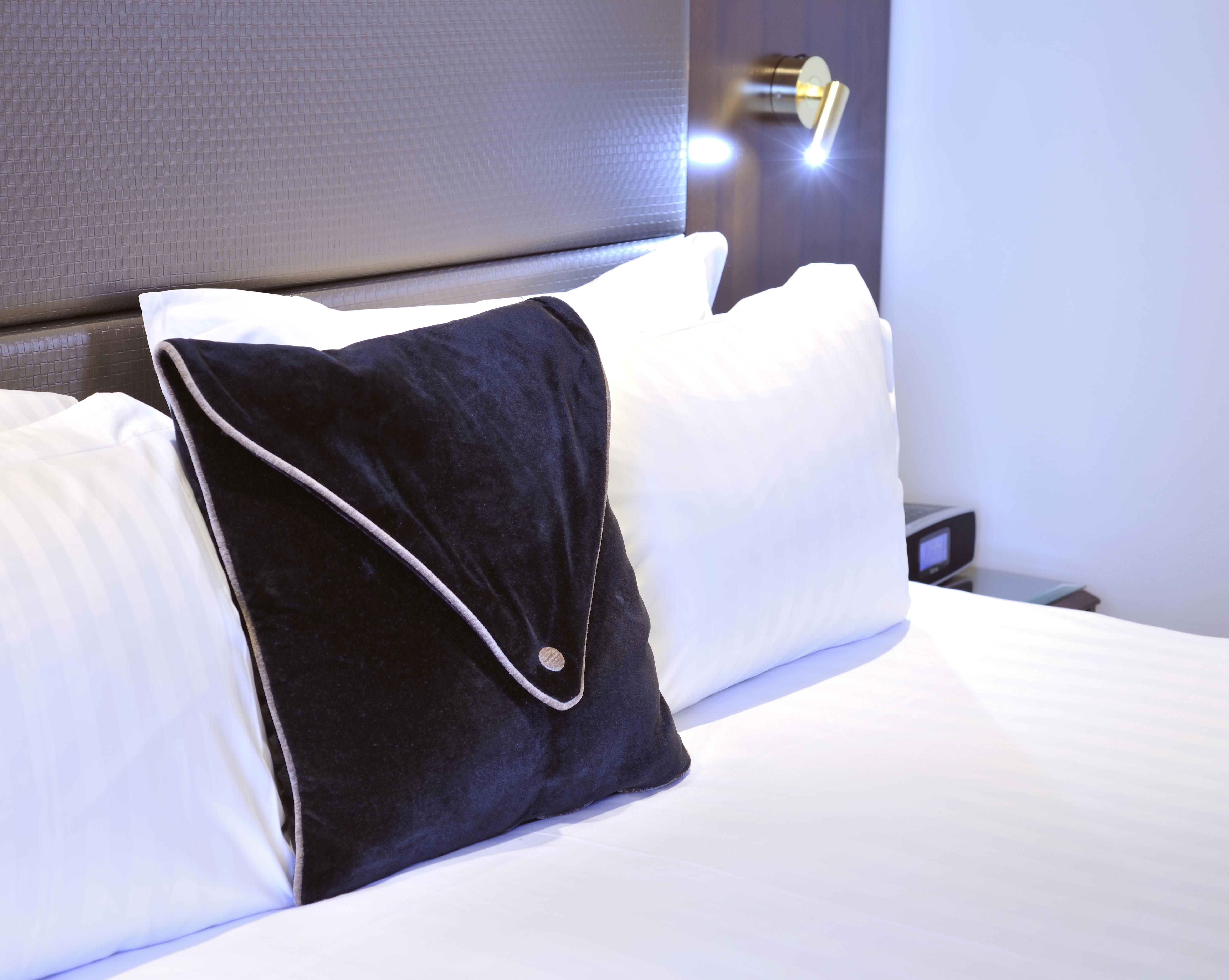 Hotel Stamford Plaza Ville de Melbourne Extérieur photo The photo shows a neatly arranged bed with white linens. There are several pillows, with one black pillow featuring a distinctive design on top of the white pillows. The headboard of the bed is visible, along with a stylish wall-mounted light fixture