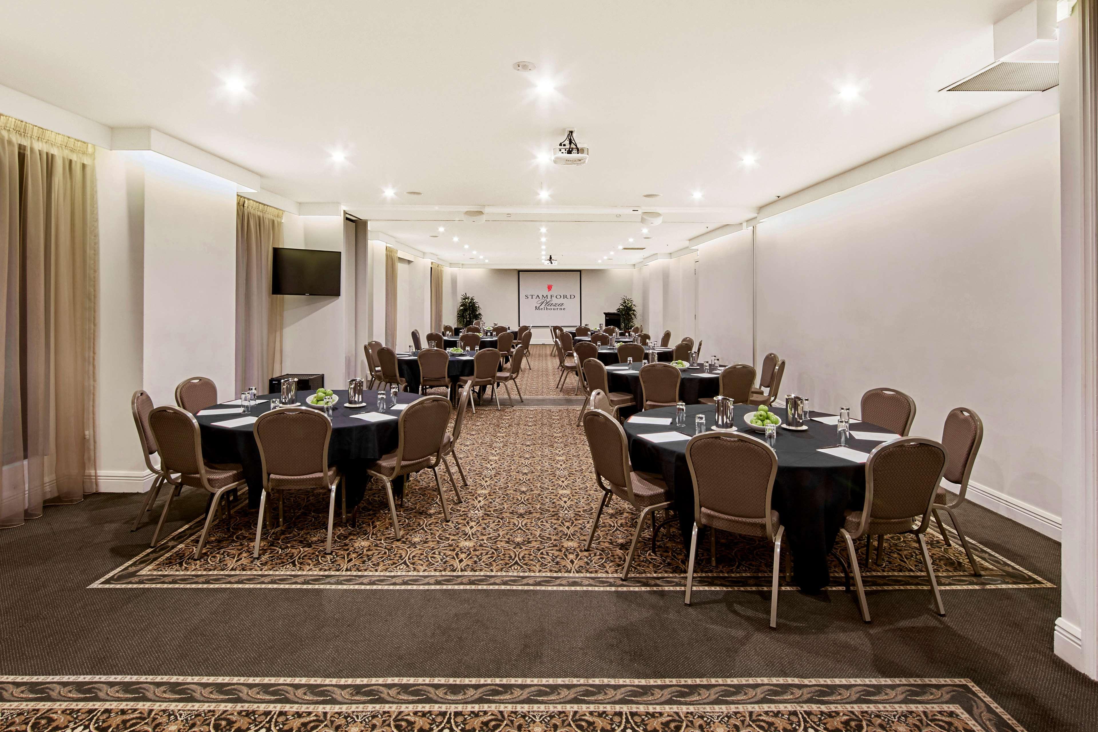 Hotel Stamford Plaza Ville de Melbourne Extérieur photo The photo shows an event space or banquet hall set up for a gathering. The room features several round tables covered with black tablecloths, each adorned with small centerpieces. Chairs are arranged around each table. The lighting is bright and mode
