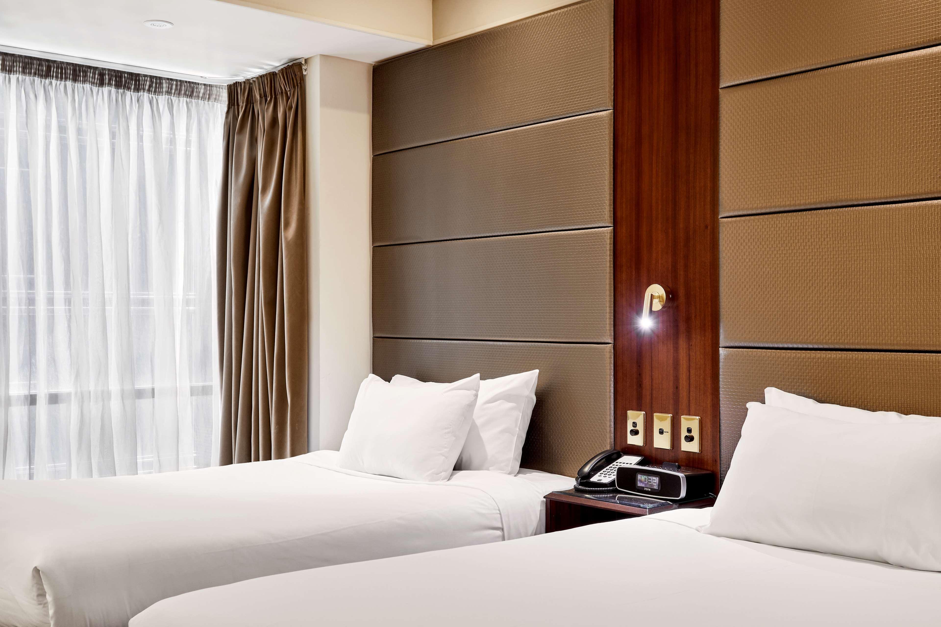 Hotel Stamford Plaza Ville de Melbourne Extérieur photo The photo shows a modern hotel room featuring two twin beds with white linens and fluffy pillows. The walls behind the beds have a combination of textured panels in neutral colors. There is a bedside table with a lamp and a phone. A large window with