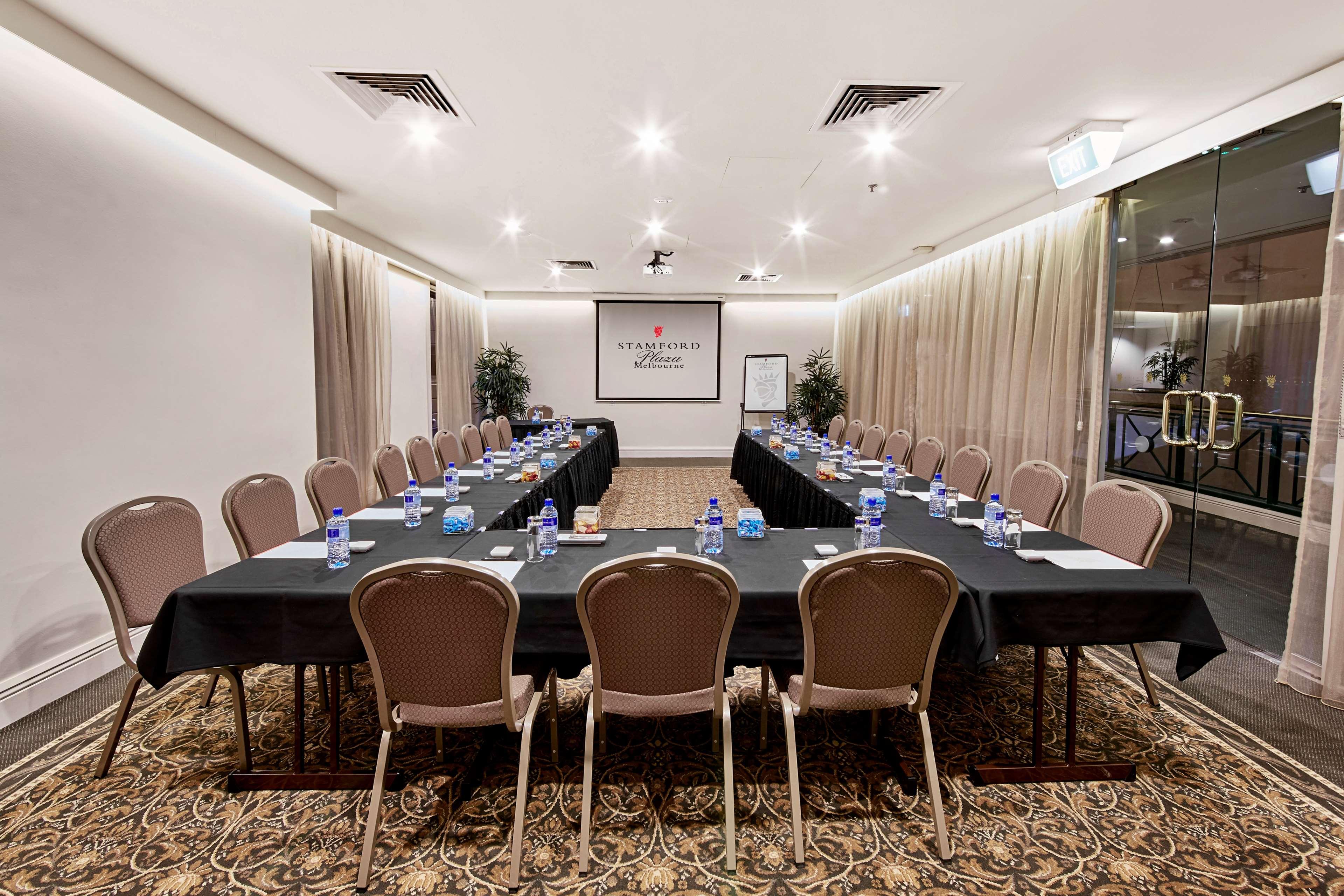 Hotel Stamford Plaza Ville de Melbourne Extérieur photo The photo shows a conference room set up for a meeting. There are several long tables arranged in a U-shape, covered with black tablecloths. Each table has a water bottle and notepad placed at intervals. The room is well-lit, with light-colored walls