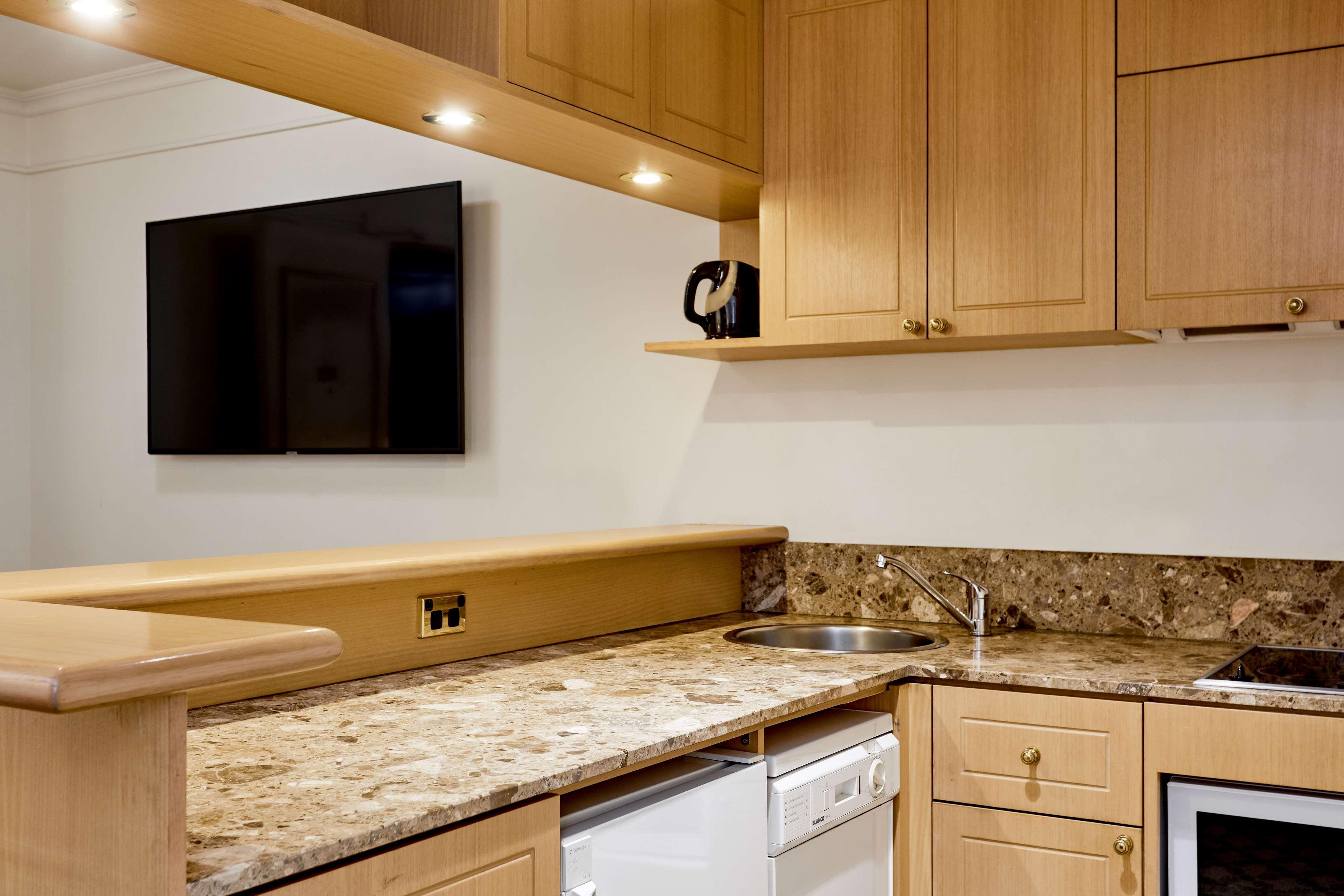 Hotel Stamford Plaza Ville de Melbourne Extérieur photo The photo shows a modern kitchen with wooden cabinetry and a granite countertop. There's a stainless steel sink integrated into the countertop, and appliances including a dishwasher and possibly a coffee maker on the shelf above. A flat-screen televi