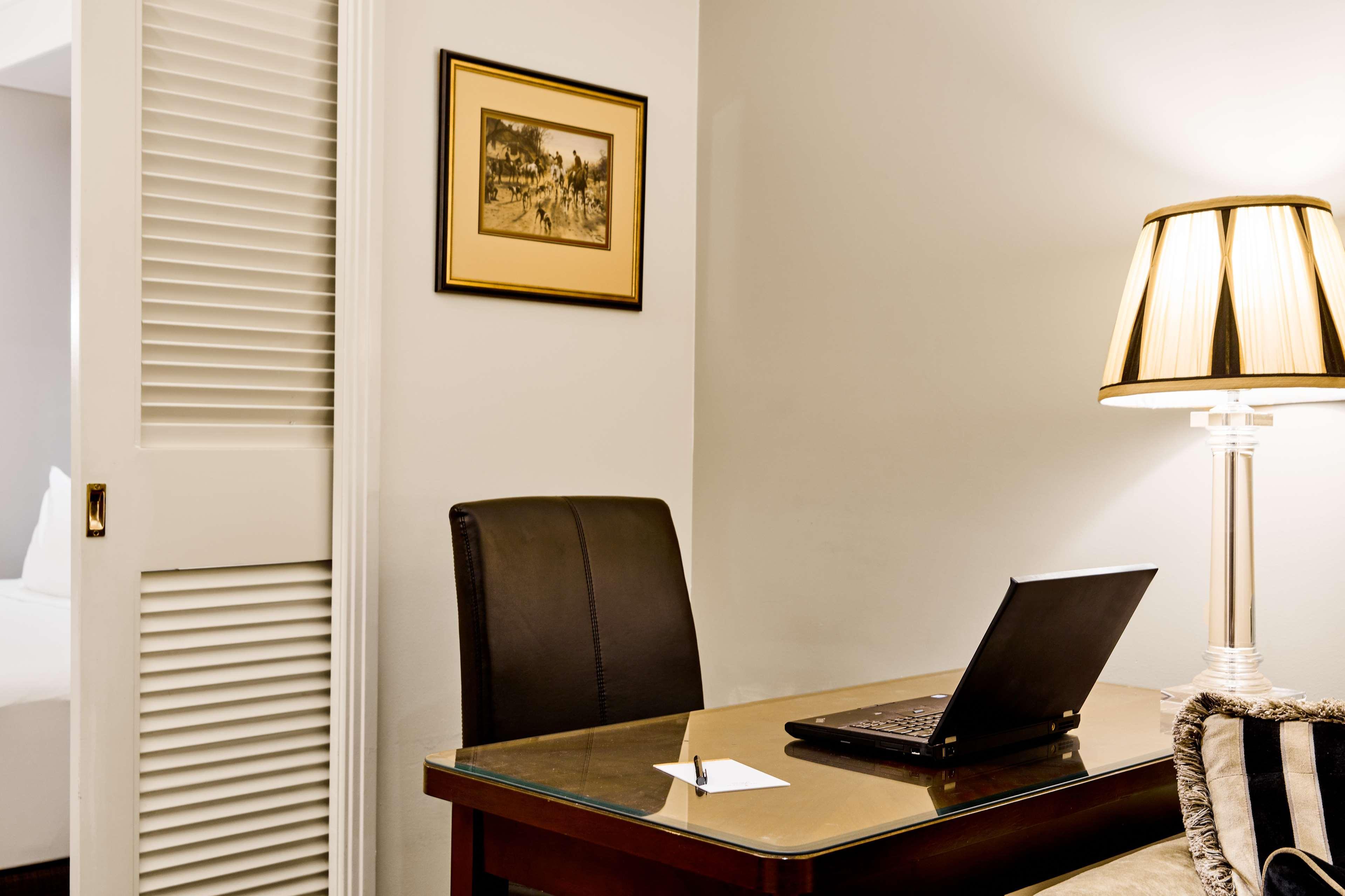 Hotel Stamford Plaza Ville de Melbourne Extérieur photo The photo shows a small office or workspace. There is a desk with a glass surface, and on it sits a laptop computer. A piece of paper or notecard is also placed on the desk. Behind the desk is a black office chair. A wall lamp with a striped shade is