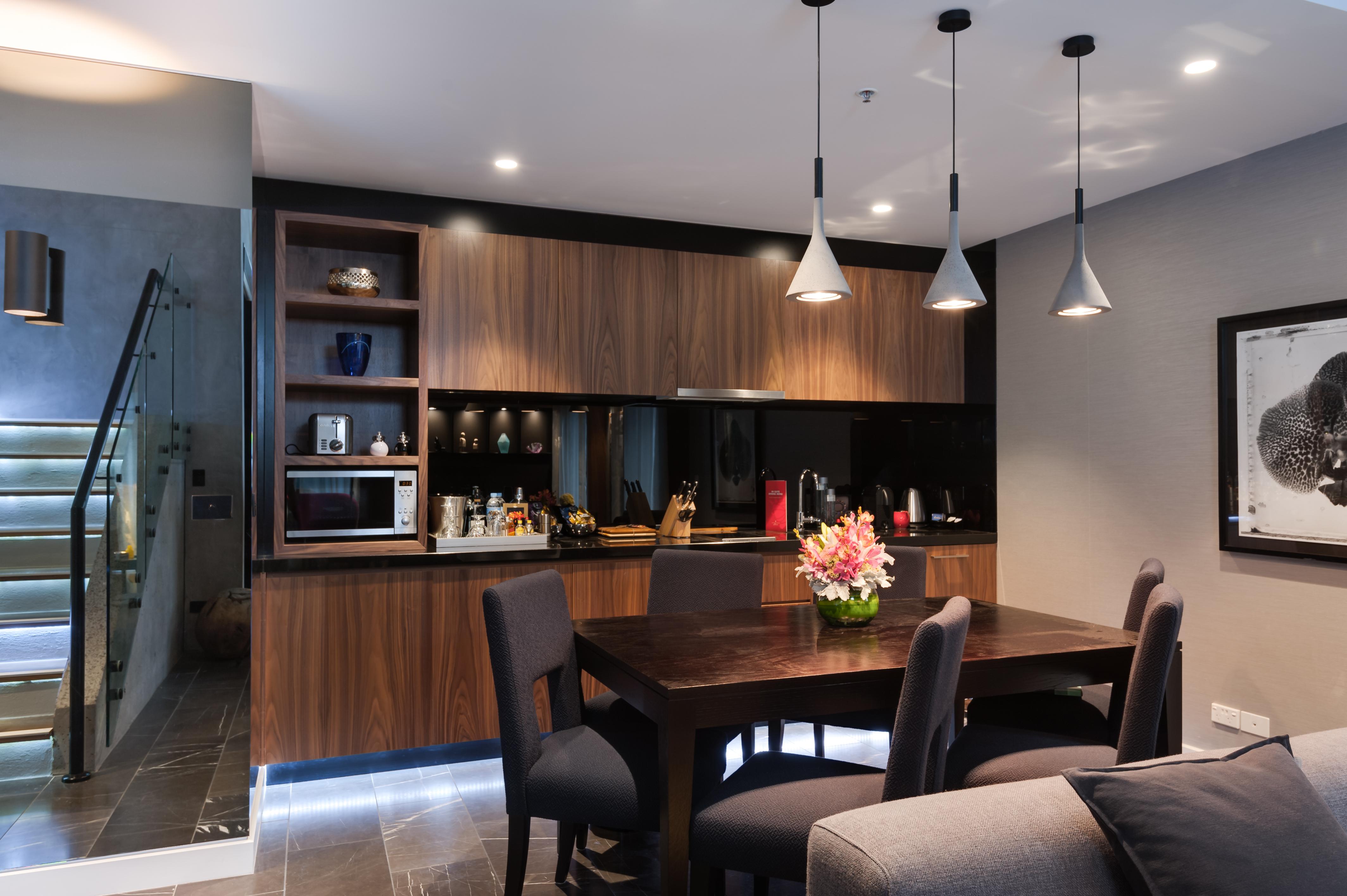 Hotel Stamford Plaza Ville de Melbourne Extérieur photo The image shows a modern kitchen and dining area. The kitchen features dark wooden cabinetry with black accents, a microwave, and various kitchen items arranged on the shelves. There is a dining table made of dark wood, surrounded by several chairs. 