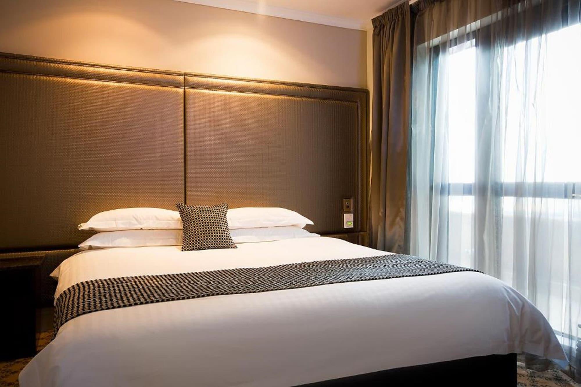 Hotel Stamford Plaza Ville de Melbourne Extérieur photo The photo shows a modern bedroom featuring a large bed with a neatly arranged white comforter and decorative pillows. The headboard is upholstered in a dark material, and there is soft lighting above it. On one side of the bed, there’s a small decora