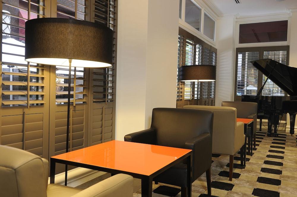 Hotel Stamford Plaza Ville de Melbourne Extérieur photo The photo shows a cozy interior space, likely a lounge or café. It features a modern design with a mix of seating options, including black and light-colored chairs surrounding small tables. One table has a bright orange top, creating a striking visua