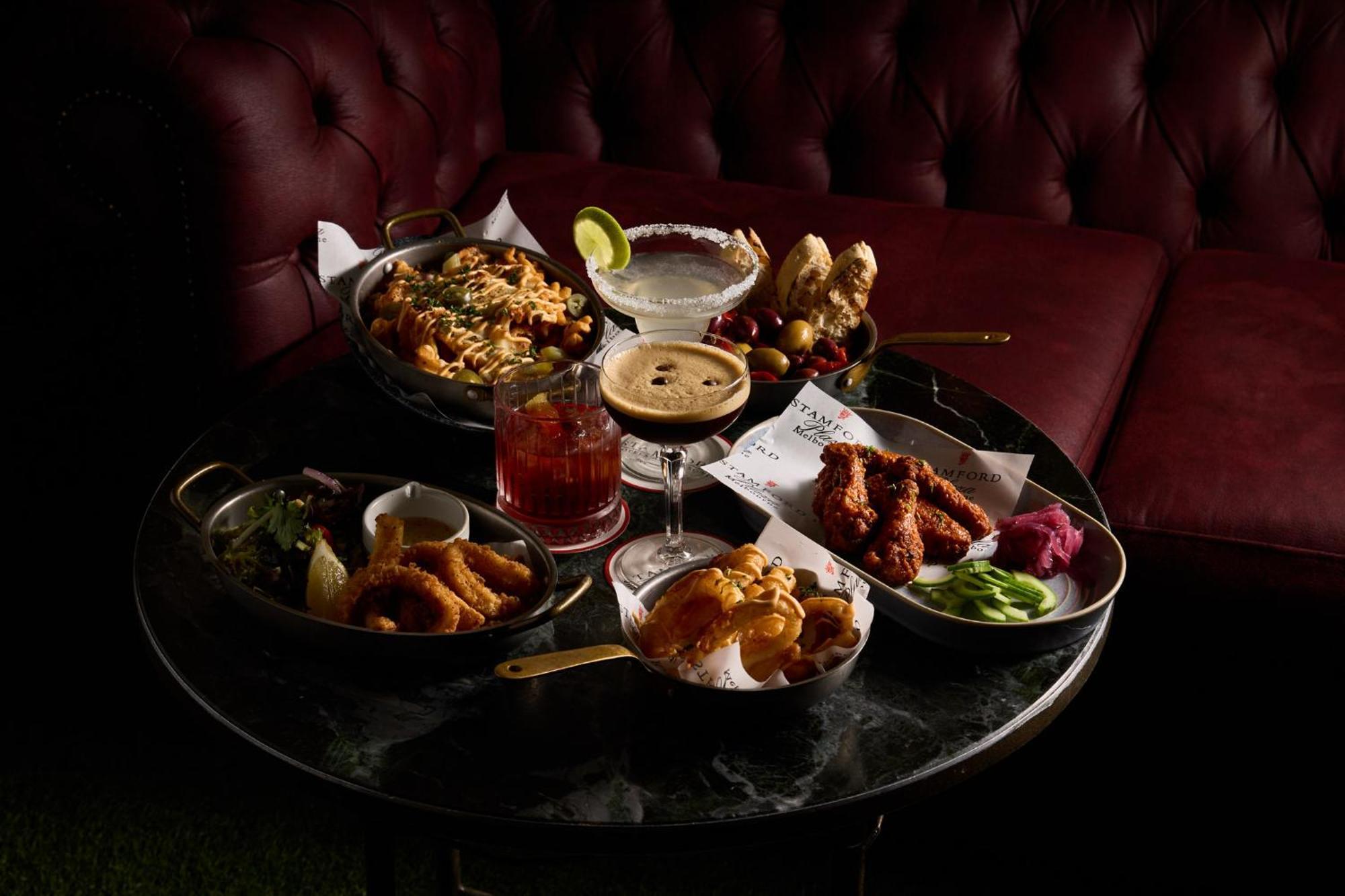 Hotel Stamford Plaza Ville de Melbourne Extérieur photo The photo showcases a variety of delicious foods and drinks arranged on a dark marble table. There are several dishes including:

1. A large bowl of pasta with a creamy sauce.
2. A platter of chicken wings, likely spicy or barbecued.
3. A small salad