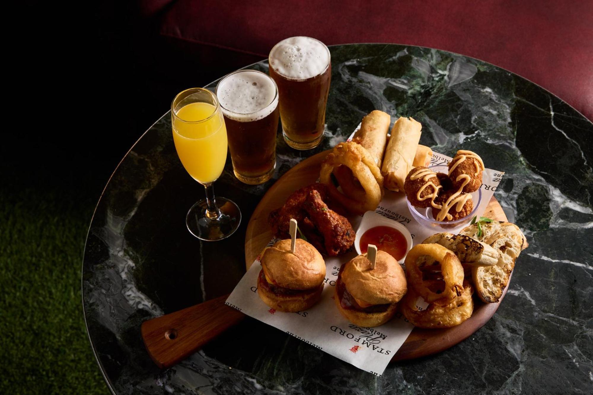 Hotel Stamford Plaza Ville de Melbourne Extérieur photo The photo displays a variety of food and drinks arranged on a marble table. There are small burgers garnished with skewers, crispy chicken pieces, and deep-fried snacks. Additionally, there are two glasses of beer and a cocktail, likely a mimosa, pre