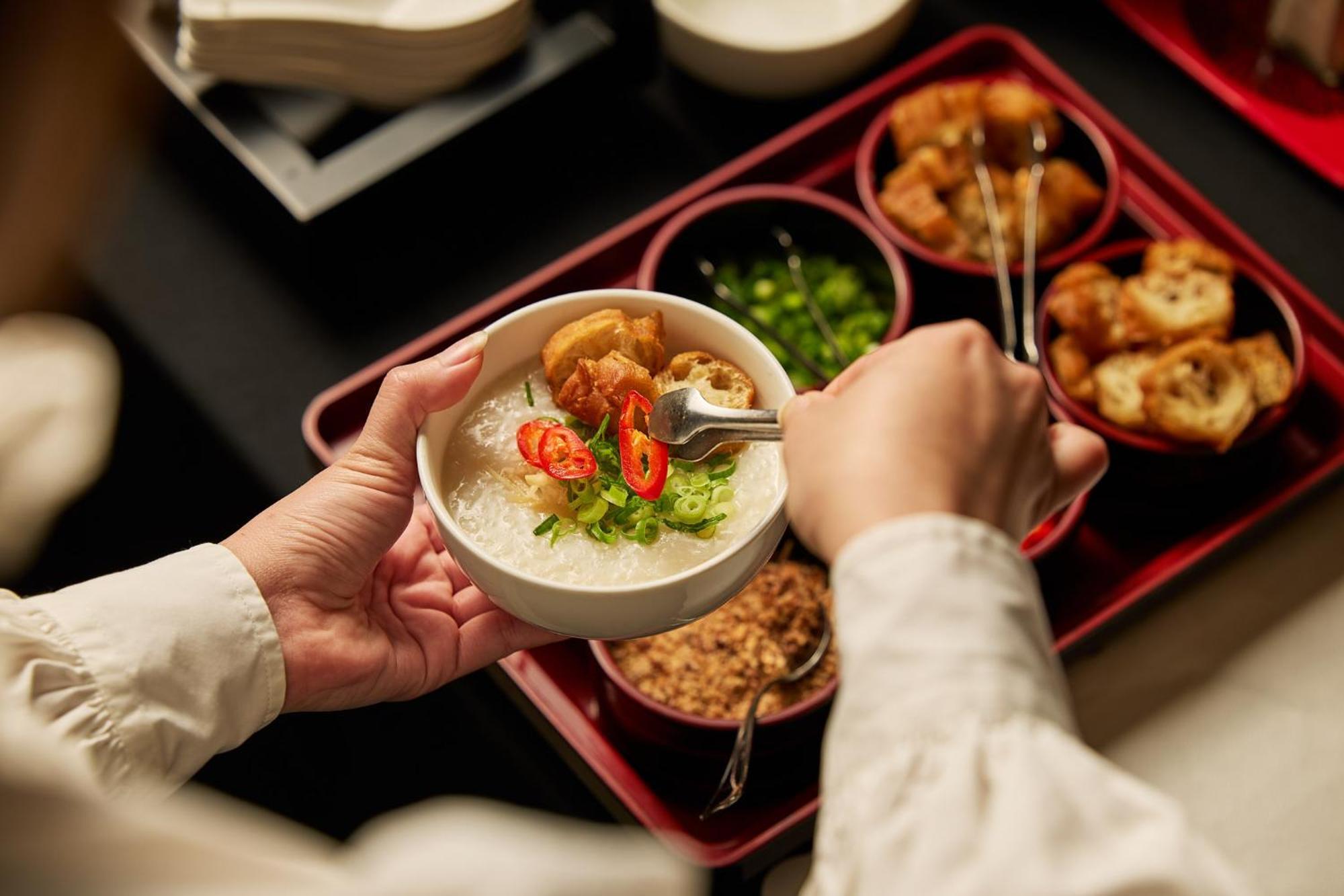 Hotel Stamford Plaza Ville de Melbourne Extérieur photo The photo shows a person serving food from a tray filled with various dishes. In one hand, they are holding a bowl filled with a creamy, likely rice-based dish topped with slices of chili and possibly fried tofu or other toppings. Surrounding the bow