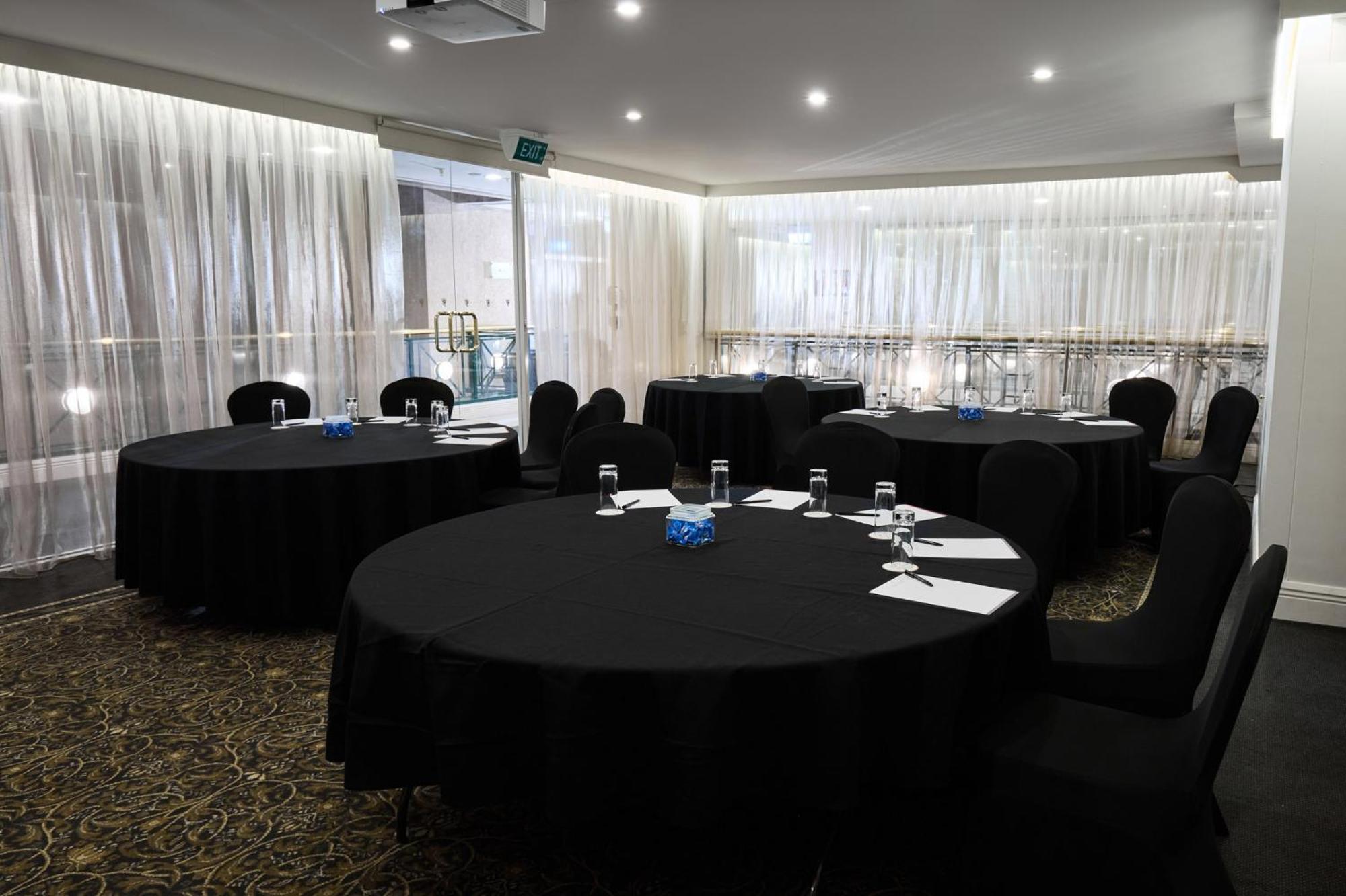 Hotel Stamford Plaza Ville de Melbourne Extérieur photo The photo shows a meeting or conference room set up with several round tables covered in black tablecloths. Each table is accompanied by black chairs. There are some white notepads and pens placed on the tables, and a small decorative item, possibly 