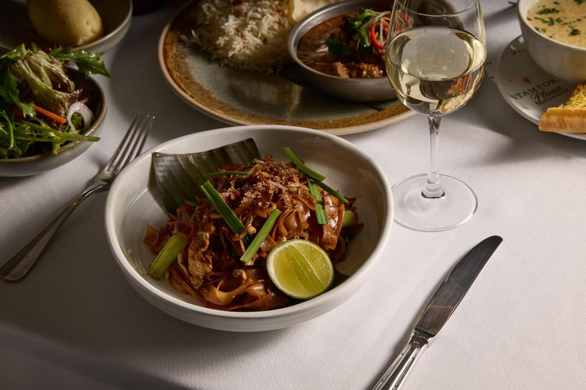 Hotel Stamford Plaza Ville de Melbourne Extérieur photo The photo features a beautifully arranged dining table with several dishes. In the foreground, there is a bowl of noodles topped with green onions and garnished with a lime wedge. The noodles appear to be stir-fried and have a rich color. Next to the