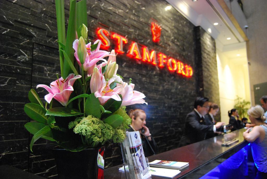 Hotel Stamford Plaza Ville de Melbourne Extérieur photo The photo shows a hotel reception area with a prominent sign that reads "STAMFORD" in bright red letters. In the foreground, there is a decorative arrangement of flowers, primarily featuring pink lilies, along with greenery. The reception counter is 